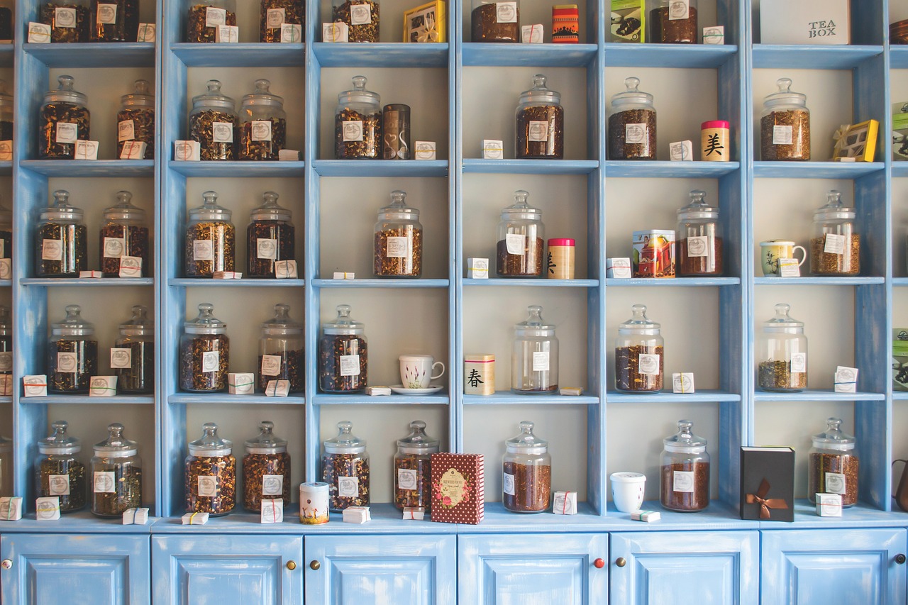 Wall of blue wooden shelves filled with glass jars containing various dried herbs and natural remedies for apothecary or herbal medicine use.