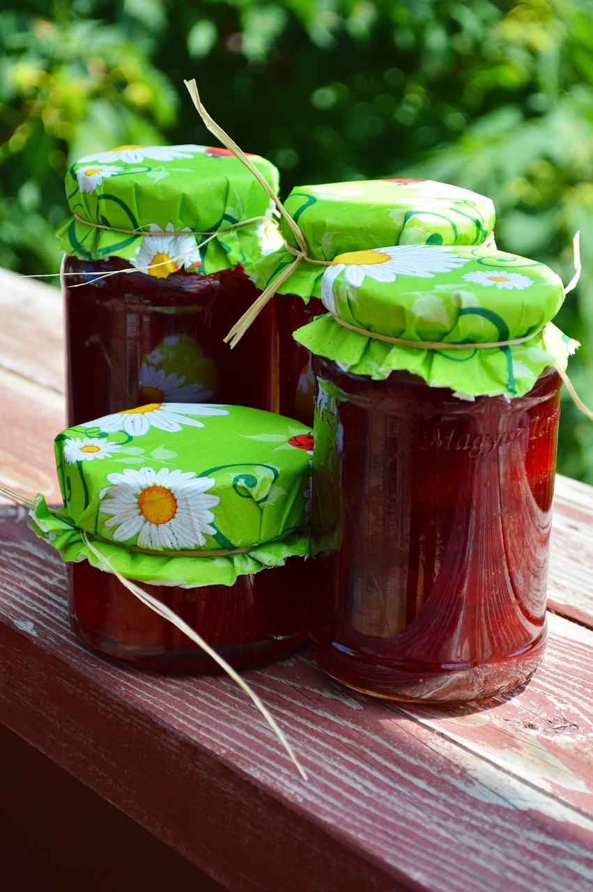 Jars of homemade jam sealed with green floral fabric and tied with raffia, sitting on a wooden surface in natural sunlight—perfect for illustrating home canning basics.