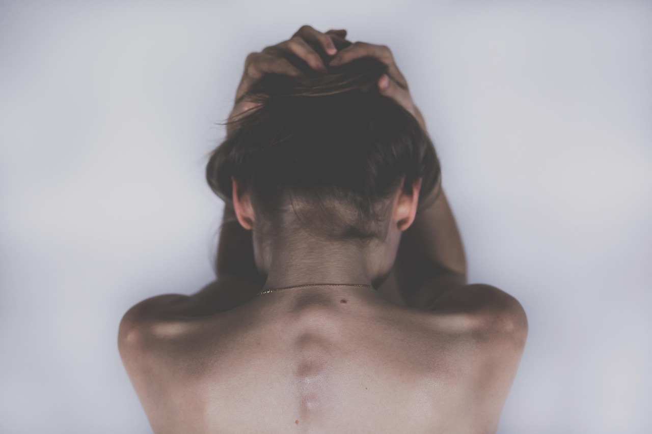 Woman sitting with her back exposed and head in hands, symbolizing emotional struggle and the weight of postpartum depression.